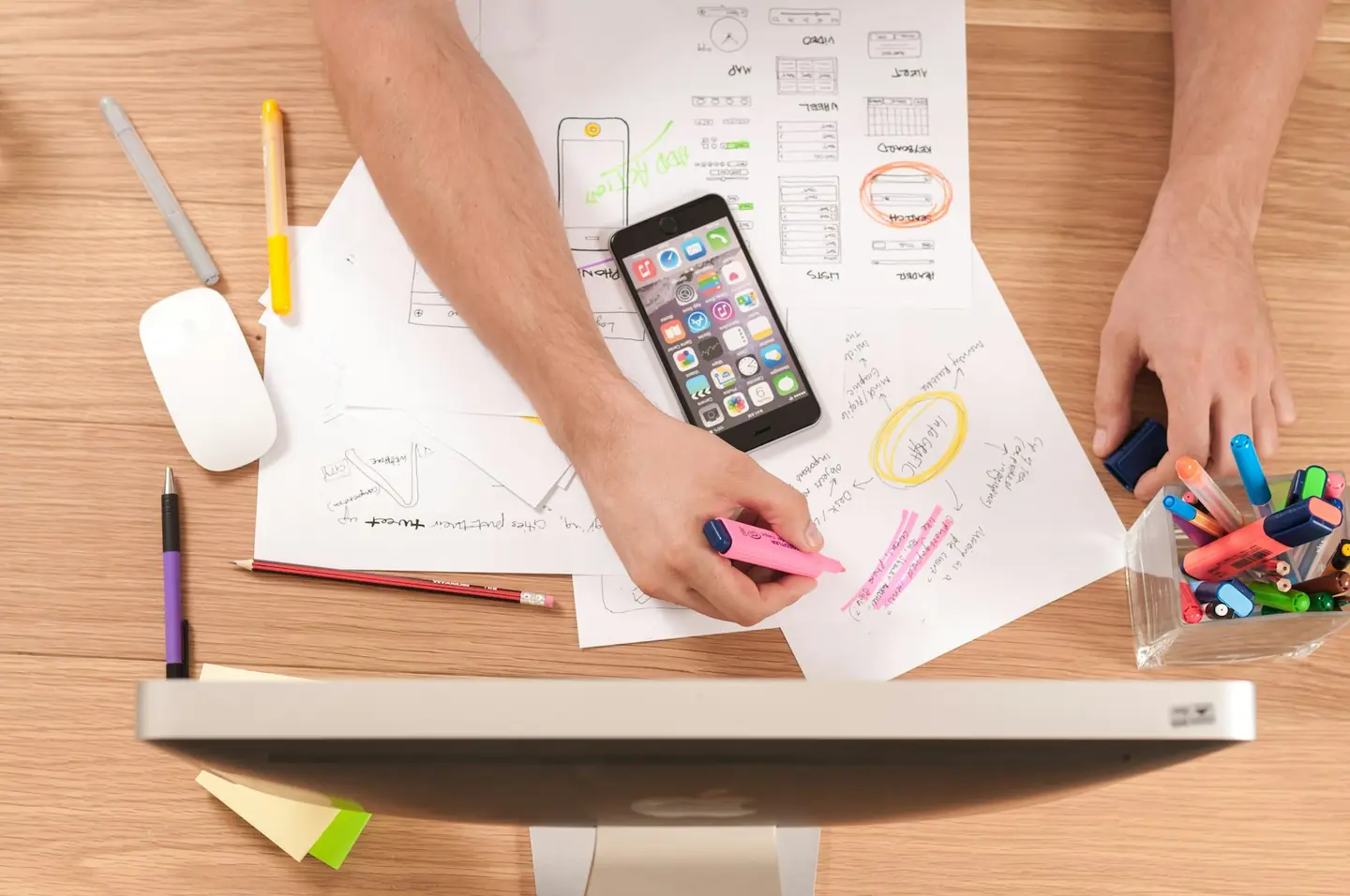Designer sketching mobile app wireframes on paper beside a phone